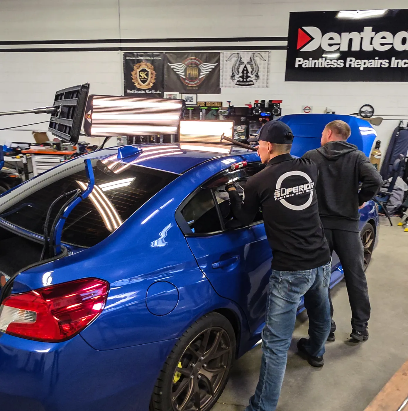 Jay Ma 在 Dented 廠內燈板下修復藍色轎車的冰雹凹痕